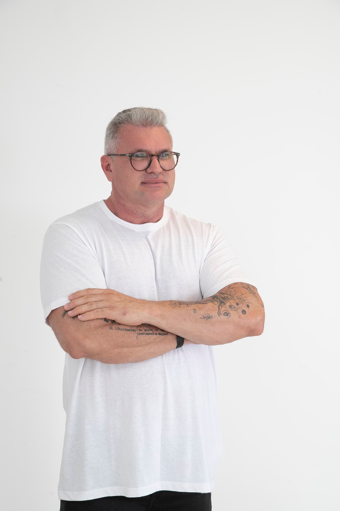 Julian Lemos em retrato de estúdio, com camiseta branca e tatuagens à mostra